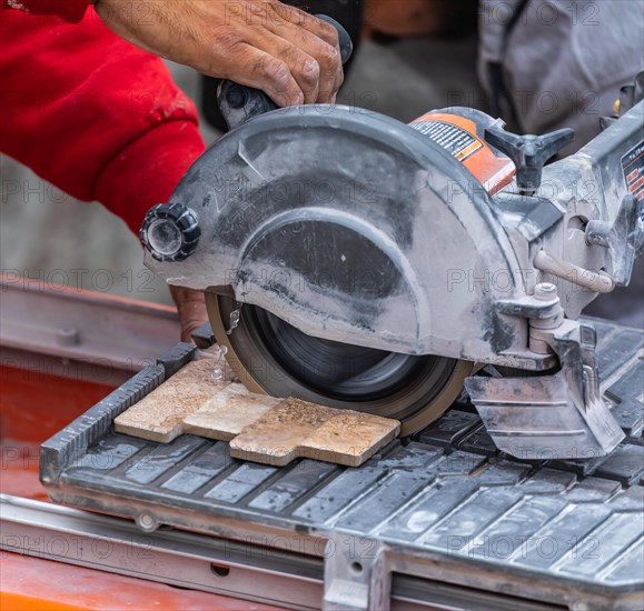 Worker using wet tile saw to cut wall tile at construction site