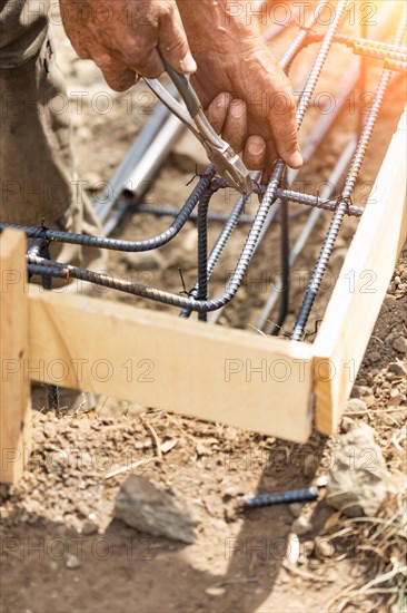 Worker securing steel rebar framing with wire plier cutter tool at construction site