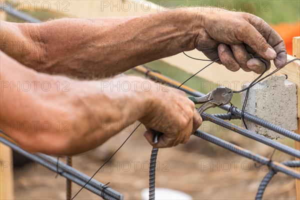 Worker securing steel rebar framing with wire plier cutter tool at construction site