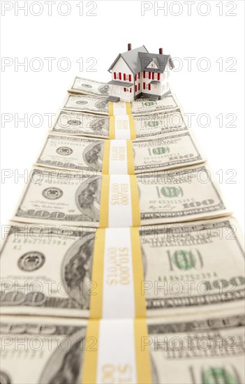 Small house on row of hundred dollar bill stacks isolated on a white background