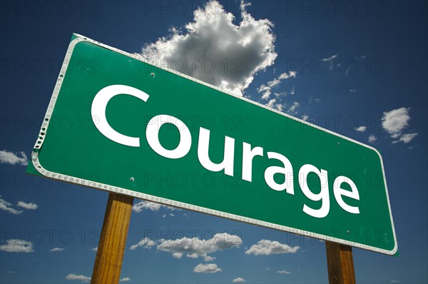 Courage green road sign over dramatic clouds and sky