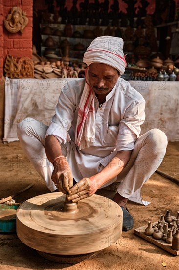 Indian potter at work: throwing the potter's wheel and shaping ceramic vessel and clay ware: pot