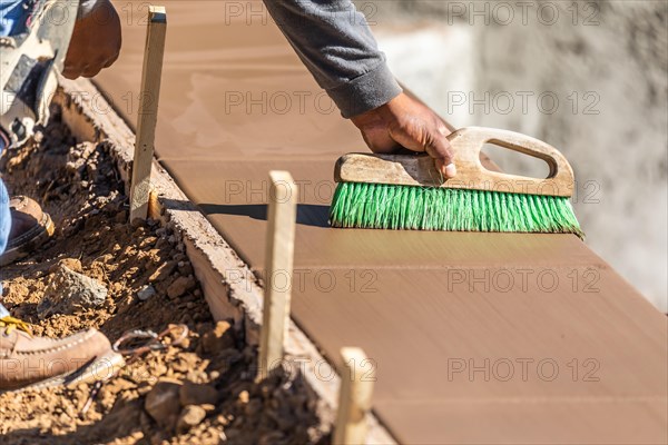 Construction worker using brush on wet cement forming coping around new pool