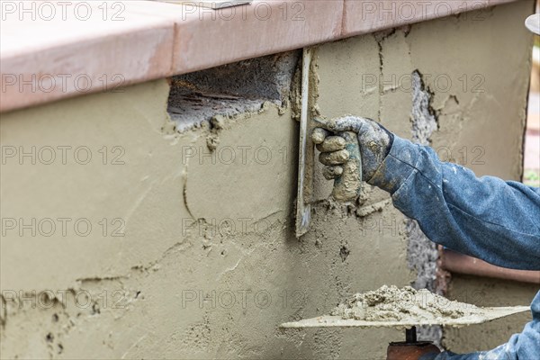 Tile worker applying cement with trowel at pool construction site