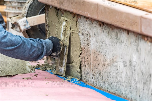 Tile worker applying cement with trowel at pool construction site