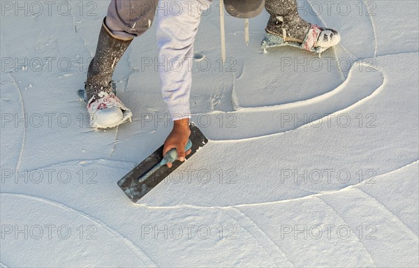 Worker wearing spiked shoes smoothing wet pool plaster with trowel