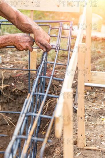 Worker securing steel rebar framing with wire plier cutter tool at construction site