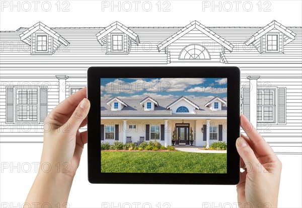 Female hands holding computer tablet with house photo on screen & drawing behind