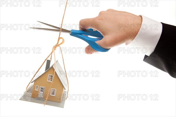 Hand with scissors cutting string holding house isolated on a white background