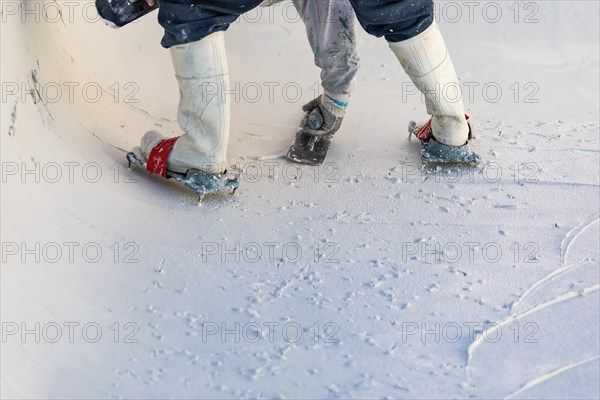 Worker wearing spiked shoes smoothing wet pool plaster with trowel