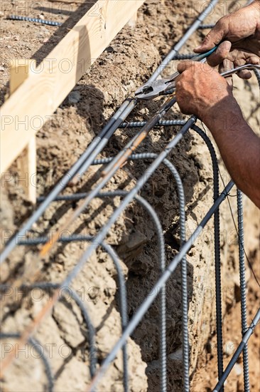 Worker securing steel rebar framing with wire plier cutter tool at construction site