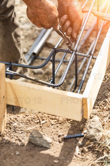 Worker securing steel rebar framing with wire plier cutter tool at construction site