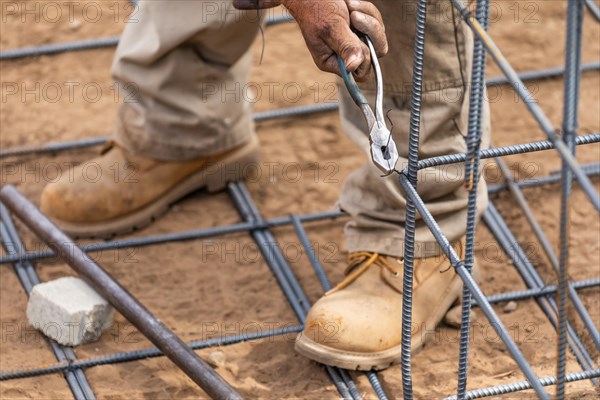 Worker securing steel rebar framing with wire plier cutter tool at construction site