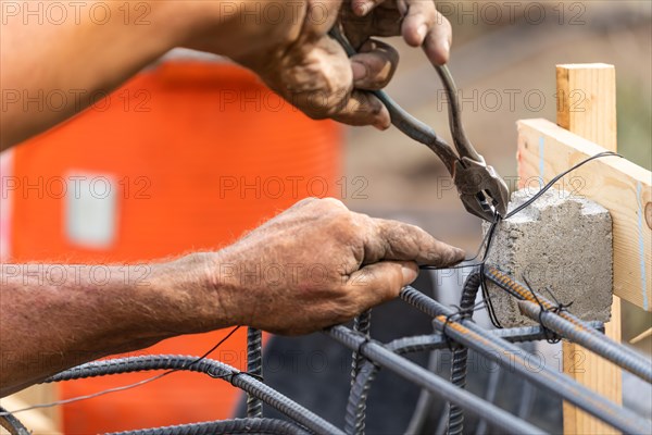 Worker securing steel rebar framing with wire plier cutter tool at construction site