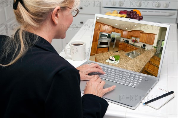 Woman in kitchen using laptop to research home improvement ideas. screen can be easily used for your own message or picture. picture on screen is my copyright as well