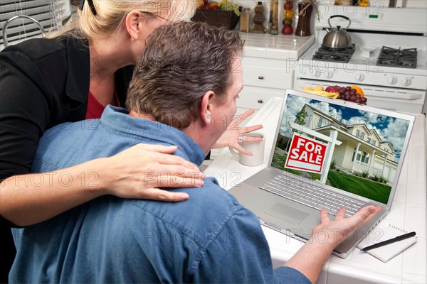 Couple in kitchen using laptop to research real estate. screen can be easily used for your own message or picture. picture on screen is my copyright as well