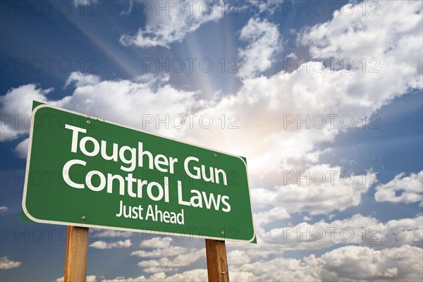 Tougher gun control laws green road sign with dramatic clouds and sky