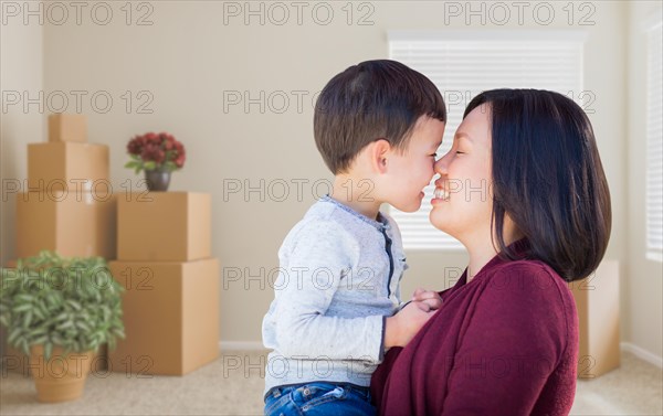 Young mixed-race chinese mother and child in empty room with packed moving boxes and plants
