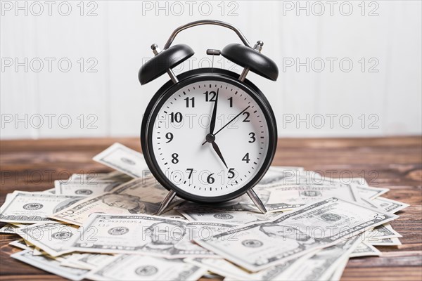 Alarm clock on spread currency notes over wooden textured background