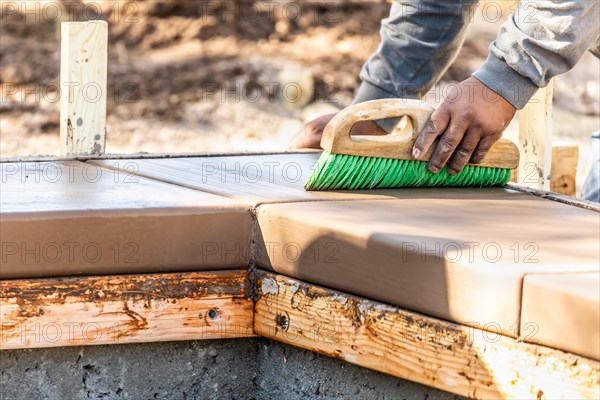 Construction worker using brush on wet cement forming coping around new pool