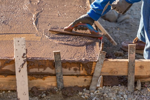 Construction worker smoothing wet cement with trowel tools