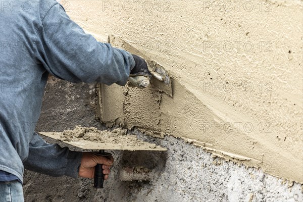 Tile worker applying cement with trowel at pool construction site