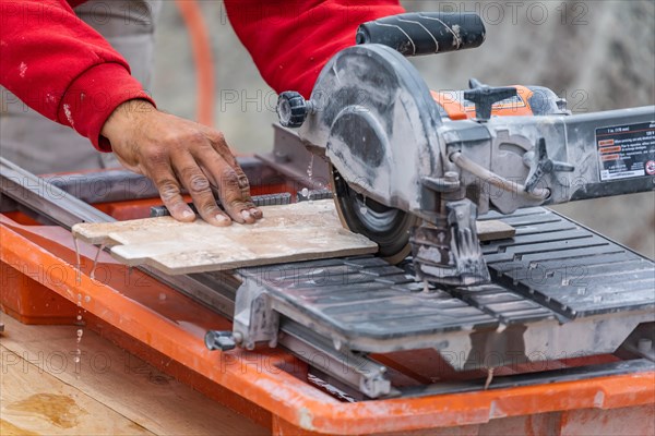 Worker using wet tile saw to cut wall tile at construction site