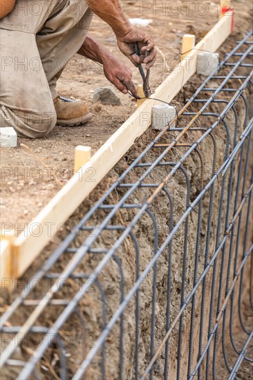 Worker securing steel rebar framing with wire plier cutter tool at construction site