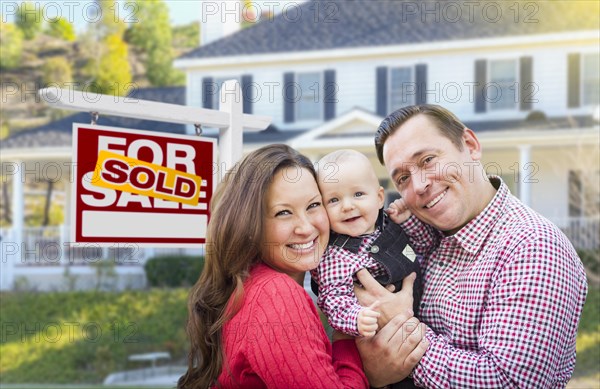 Happy young family in front of for sale real estate sign and house