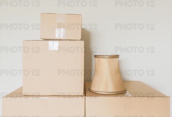 Variety of packed moving boxes and lamp shade in empty room against wall