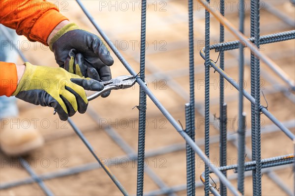 Worker securing steel rebar framing with wire plier cutter tool at construction site