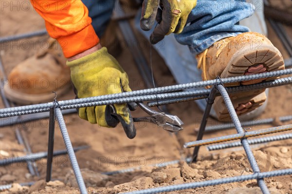 Worker securing steel rebar framing with wire plier cutter tool at construction site