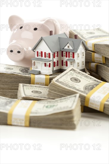 Small house and piggy bank with stacks of hundred dollar bills isolated on a white background