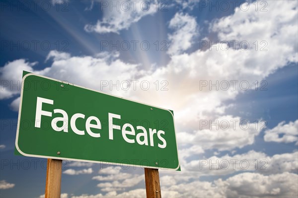 Face fears green road sign with dramatic clouds