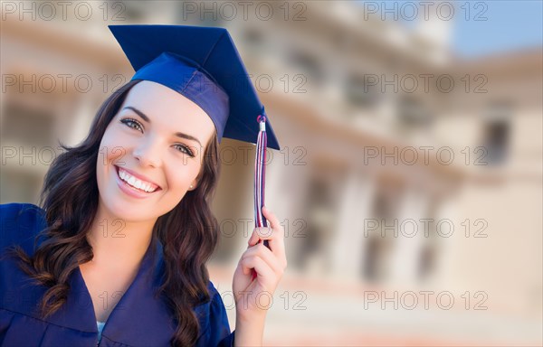 Happy graduating mixed-race woman in cap and gown celebrating on campus