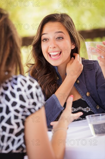 Expressive young adult woman having drinks and talking with her friend outdoors