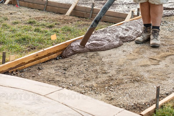 Construction worker pouring wet deck cement into wooden frame