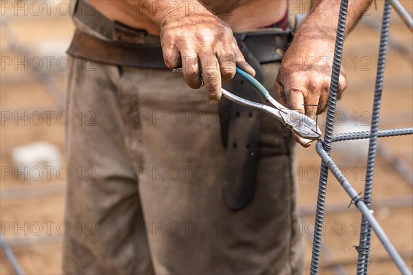 Worker securing steel rebar framing with wire plier cutter tool at construction site