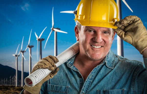 Smiling contractor in hard hat holding extention cord outdoors near wind turbines