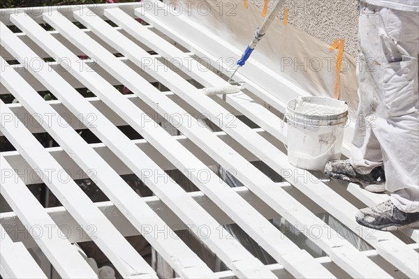 Painter rolling white paint onto the top of A home patio cover