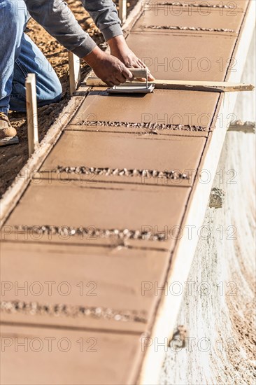 Construction worker using hand groover on wet cement forming coping around new pool