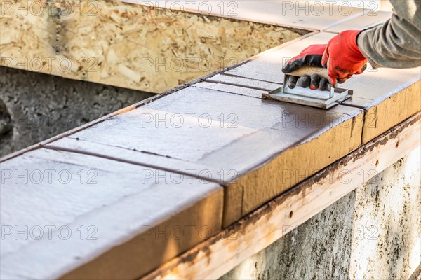 Construction worker using hand groover on wet cement forming coping around new pool