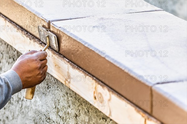 Construction worker using hand groover on wet cement forming coping around new pool