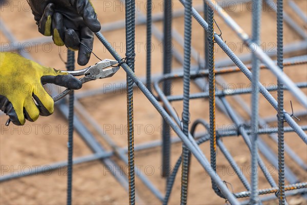 Worker securing steel rebar framing with wire plier cutter tool at construction site