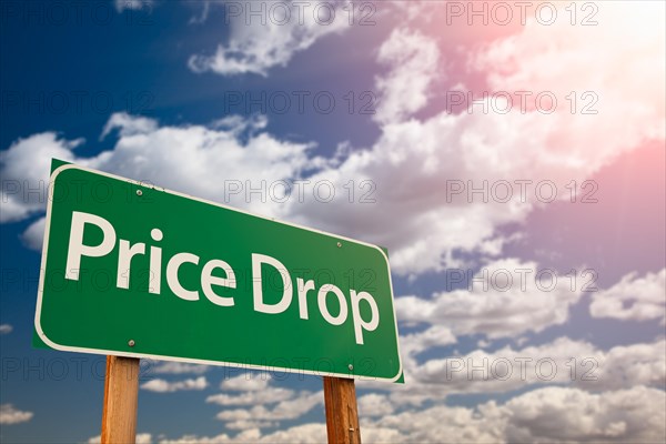 Price drop green road sign against sky