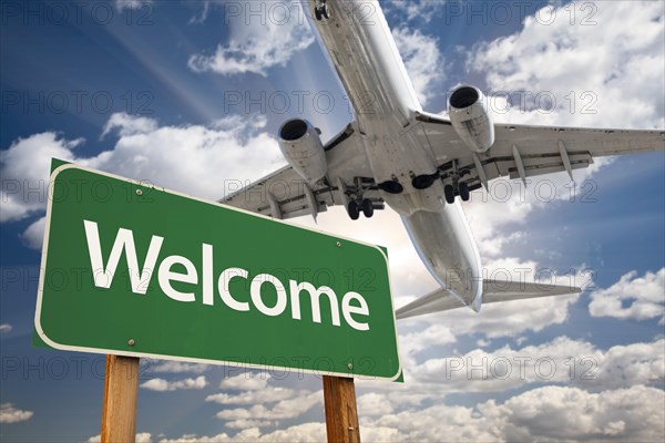 Welcome green road sign and airplane above with dramatic blue sky and clouds