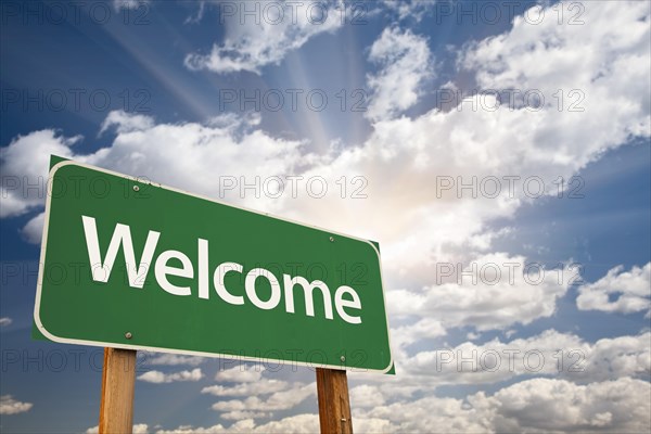 Welcome green road sign against clouds and sunburst