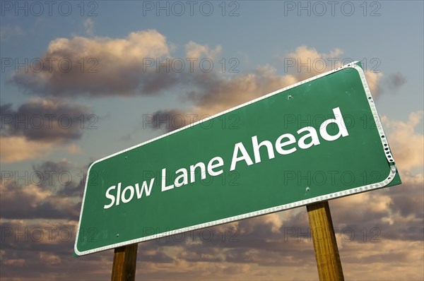 Slow lane ahead green road sign over dramatic clouds and sky