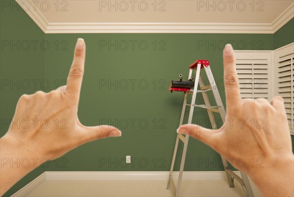 Hands framing green painted room wall interior with ladder