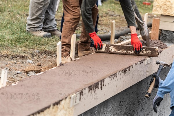 Construction workers pouring and leveling wet cement into wood framing